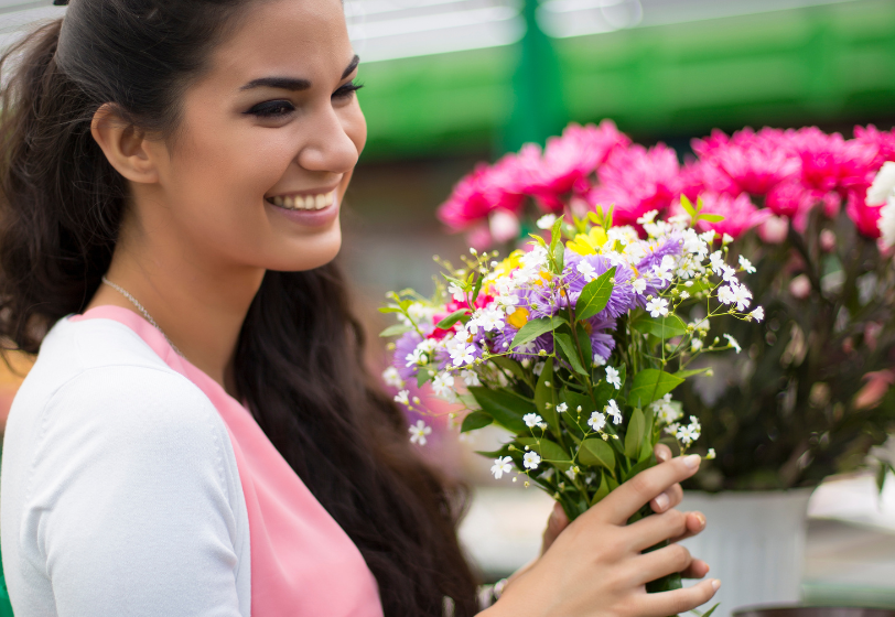 smiling woman holding flowers; who bought flowers and chose BigCommerce BOPIS option.